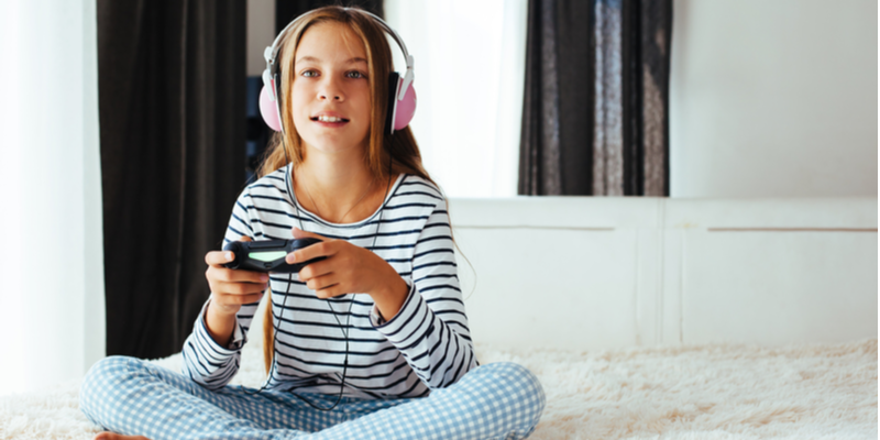 10 years old pre teen girl holding gaming console and playing on a sofa