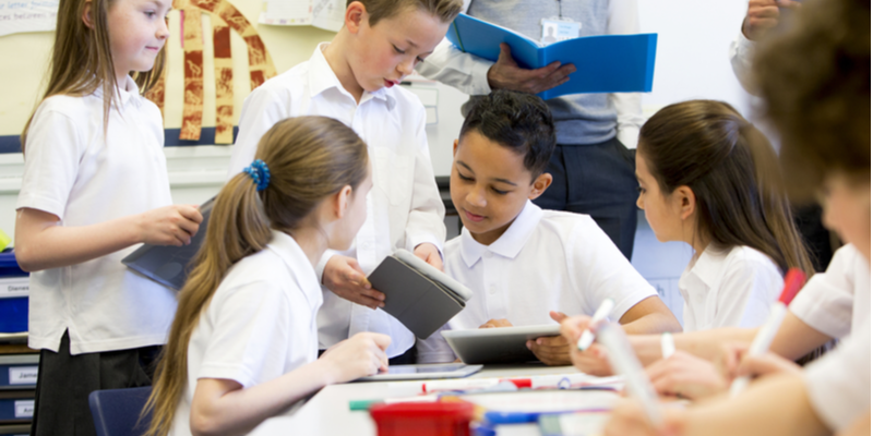 A group of school children can be seen working on digital tablets and whiteboards, they are all working happily