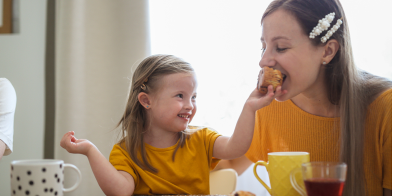 Child blond girl with Down Syndrome treats mom blonde with cupcake