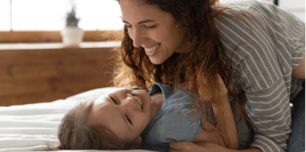 Close up cheery mother cuddles tickles little cute daughter lying in bed