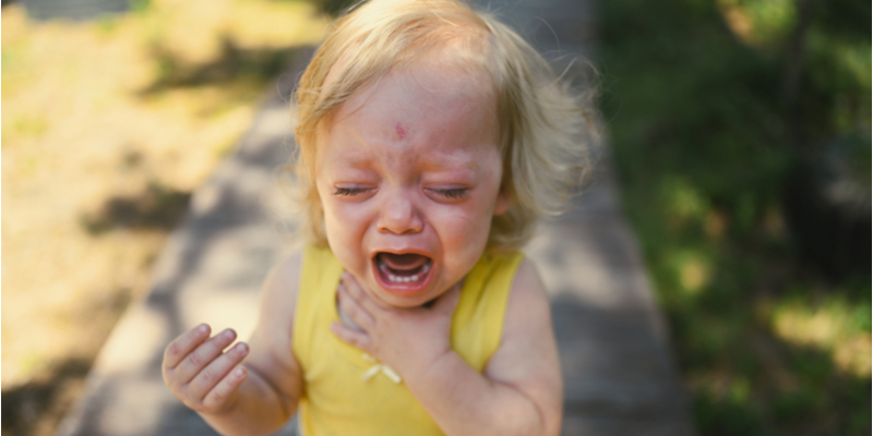 Close up portrait of little funny cute blonde girl child toddler in yellow bodysuit crying outside at summer. Childish tantrum. Healthy childhood concept