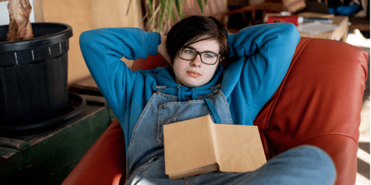 Cute androgynous teenager is lying comfortably in an armchair with a book design