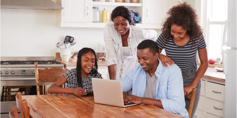 Family around kitchen table looking at laptop