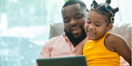 Happy family African father and little daughter sit on sofa using digital tablet playing game or watching movie together