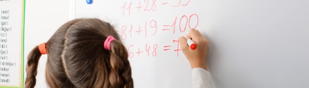 Girl does maths to class Primary school girl writing sums on whiteboard