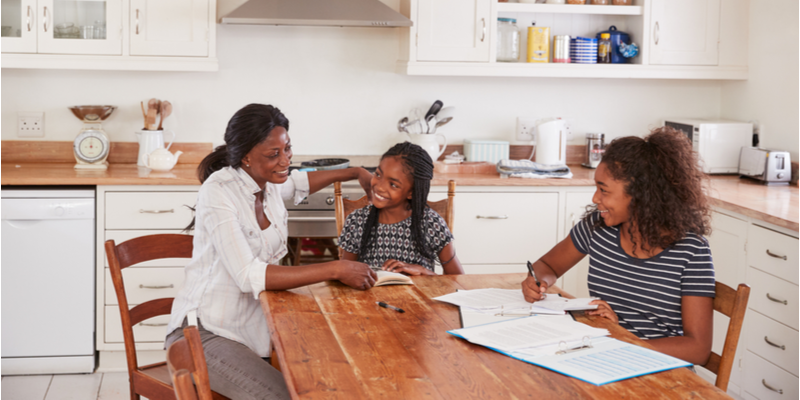 Mother helping 2 daughters sat at kitchen table