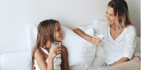 Mum and daughter relaxing in bed with glass of milk