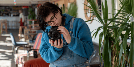 Neutral gender teen photographer taking pictures with a digital camera in a sunlit room