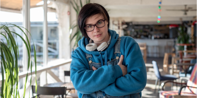 Portrait of a cute and cheerful neutral gender teenager, in a sunlit room in a cafe (1)