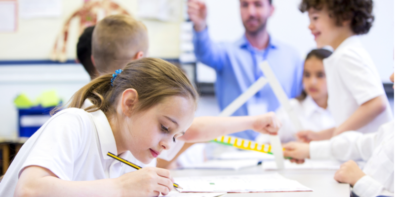 Schoolgirl sitting at a desk with other classmates while working.