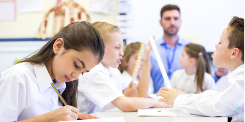 Schoolgirl sitting at a desk with other classmates while working