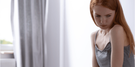 Skinny girl sitting at the table in front of a plate with hands tied with measuring tape