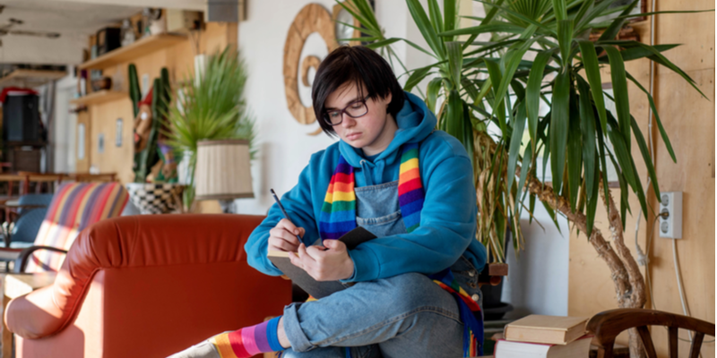 Teen androgynous girl wearing a rainbow scarf is drawing in a sketchbook