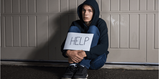 Why do young people self harm_ young teen boy sitting alone in his garage holding a help sign