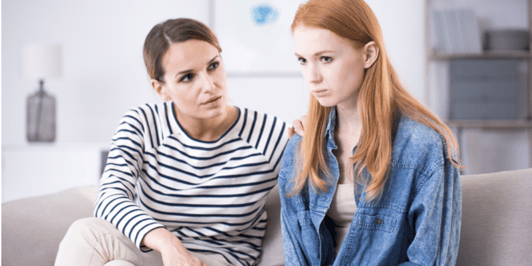 Woman comforting an emotional young teenage girl sitting with her legs crossed on a sofa and crying