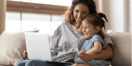 mother hug little daughter sitting on couch watching educational funny cartoons on pc laughing enjoy time together