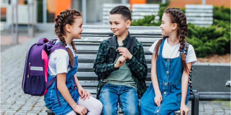 primary school. Girls and boy with backpacks near building outdoors.